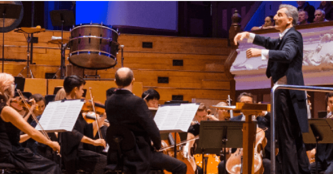 Un direttore d'orchestra che dirige l'orchestra Filarmonica di Auckland in una grande sala da concerto.